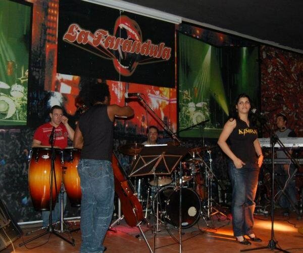 Orquesta tocando en directo con congas, batería y cantante en el escenario de la sala