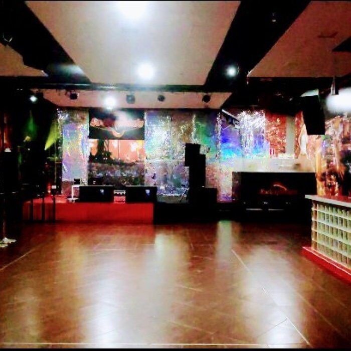 Sala vacía con pista de madera, barra iluminada en rojo y paredes con proyecciones