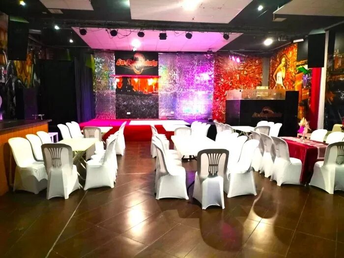 Sala montada con mesas y sillas vestidas de blanco y pasillo central alfombrado en rojo